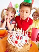 Group of adorable kids looking at birthday cake with candles, cute boy blowing on them